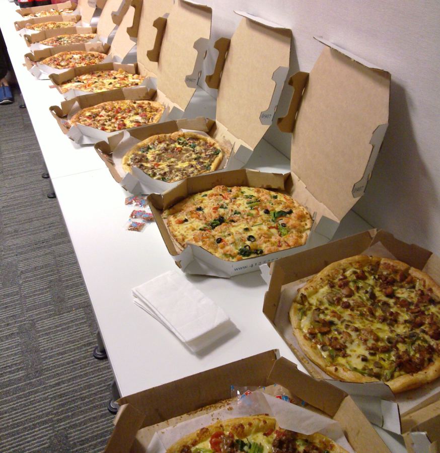 Open pizza boxes lined up on a table for an office lunch